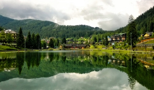 Immagine con lago, alberi, riflesso, case, montagna, acqua, nuvole, riflessi