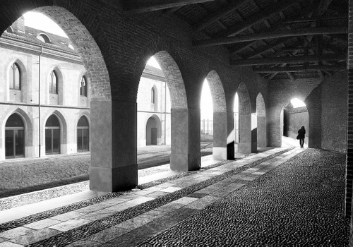 Immagine con archi, portico, travi, bianconero, finestre, persona, corridoio, colonne, ciottoli, selciato