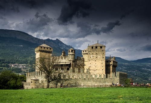 Immagine con castello, prato, verde, nuvole, torri, cielo, torre, montagna, merli, alberi
