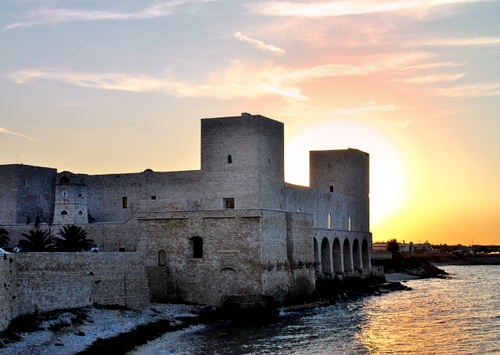 Immagine con castello, mare, torri, tramonto, acqua, sole, cielo, finestre, mura, alba, spiaggia, archi, nuvole, giallo, fortezza, riva, palme, riflesso