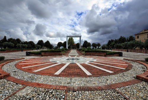 Immagine con piazza, cerchio, nuvole, sassi, cielo, alberi, arco, raggi, prospettiva, cerchi