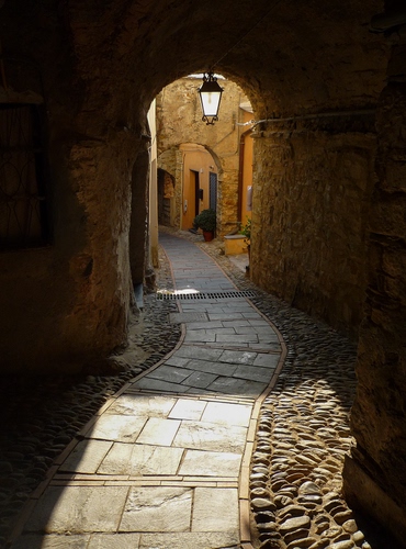 Immagine con lampione, vicolo, arco, sassi, ombra, luce, strada, ciottoli, sole