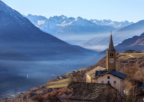 Immagine con montagne, panorama, chiesa, campanile, orologio, tetti, nebbia, neve, montagna, paesaggio, valle, borgo, vallata, lago, cielo, monti, foschia