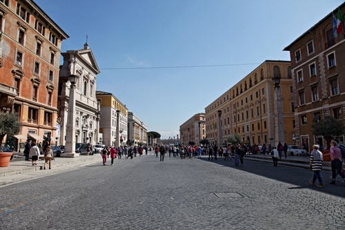 Immagine con strada, palazzi, finestre, persone, chiesa, colonne, lampioni, gente, prospettiva, tombino, piazza, case, passanti, croce, via, cielo, vasi