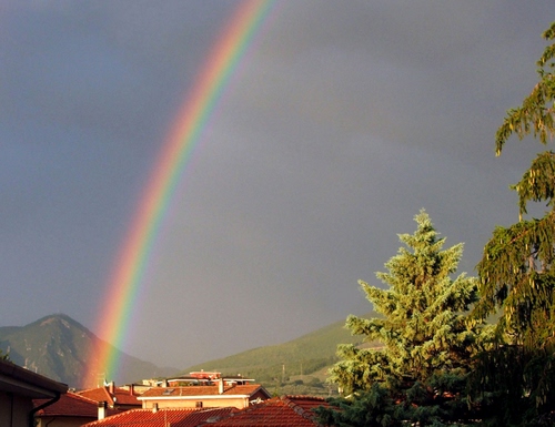 Immagine con arcobaleno, tetti, alberi, cielo, verde, colori, montagne, paesaggio, rosso, albero, case