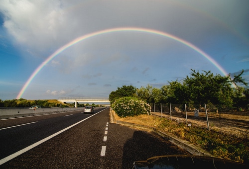 Immagine con arcobaleno, strada, cielo, alberi, nuvole, ponte, autostrada, auto, strisce, piante, automobili, arco, piazzola, guardrail, linee