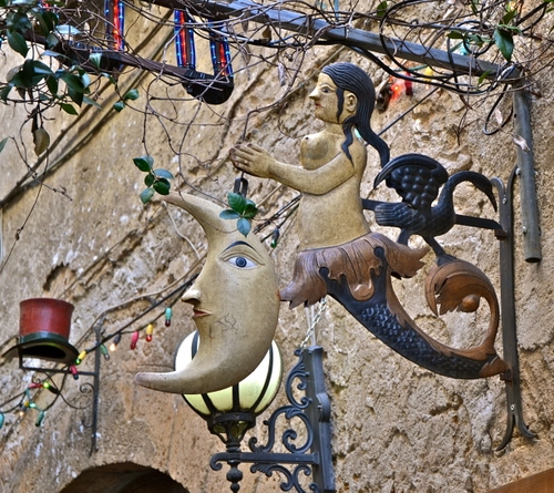 Immagine con luna, insegna, lampione, sirena, foglie, ferro, donna, arco, cappello, rami, luci, muro, vaso