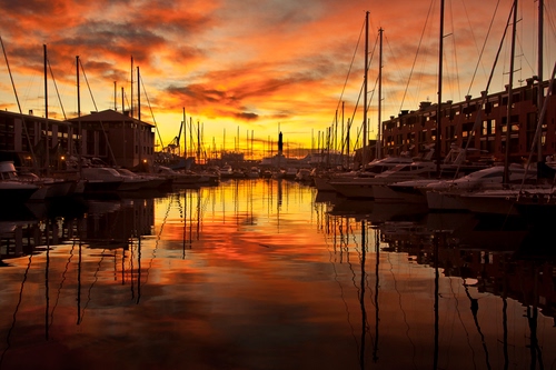 Immagine con tramonto, nuvole, barche, rosso, riflesso, cielo, acqua, porto, alberi, riflessi, giallo, canale, mare, case, arancione, imbarcazioni