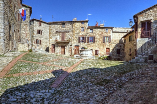 Immagine con finestre, piazza, bandiere, case, borgo, sassi, pozzo, porte, cielo