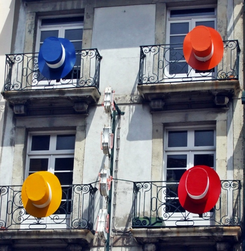 Immagine con cappelli, balconi, giallo, rosso, blu, finestre, quattro, ringhiere, arancione, arancio, colori, palazzo, porte, vetri, facciata