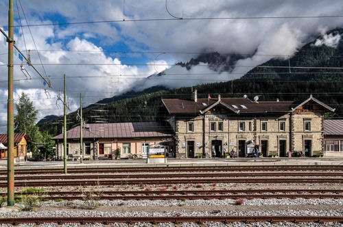 Immagine con binari, stazione, nuvole, pali, montagna, fili, alberi, ferrovia