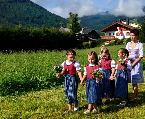 Immagine con bambini, fiori, verde, prato, montagna, bambine, campo, erba, mazzolini, case
