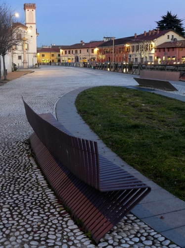 Immagine con case, panchina, piazza, aiuola, panchine, luci, torre, strada, erba, chiesa, campanile, sassi, lampioni, verde, prato, selciato, ferro