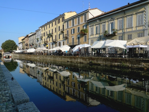 Immagine con acqua, canale, riflesso, ombrelloni, case, palazzi, cielo, riflessi, fiume, tavolini, ponte, finestre, prospettiva, mercato, bancarelle, balconi, naviglio, alberi, gazebo