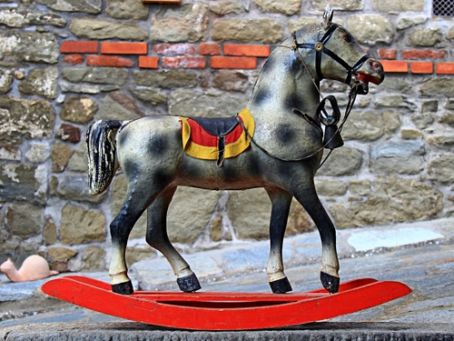 Immagine con cavallo, dondolo, giocattolo, rosso, muro, mattoni, cavallino, sella