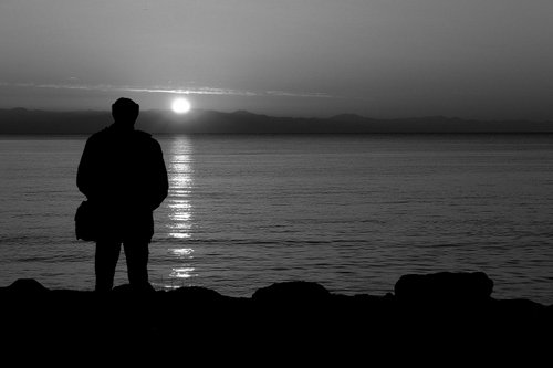 Immagine con persona, sole, controluce, mare, tramonto, riflesso, silhouette, acqua, bianconero, scogli, cielo, nero, alba, uomo, borsa, riflessi, montagne