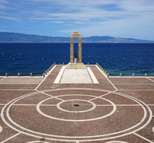 Immagine con mare, monumento, cerchi, cielo, colonne, piazza, nuvole, azzurro, montagne, acqua, geometrie, stretto, bianco, blu, statua, arena, pavimento, panorama, piazzale