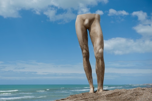 Immagine con mare, gambe, cielo, nuvole, spiaggia, sabbia, scultura, onde, azzurro, statua, ginocchia, uomo, cosce, maschio