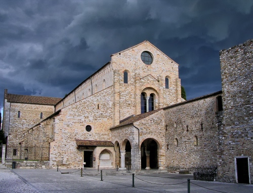 Immagine con chiesa, nuvole, piazza, colonne, bifora, archi, paletti, pietra, rosone, facciata, catena, cielo