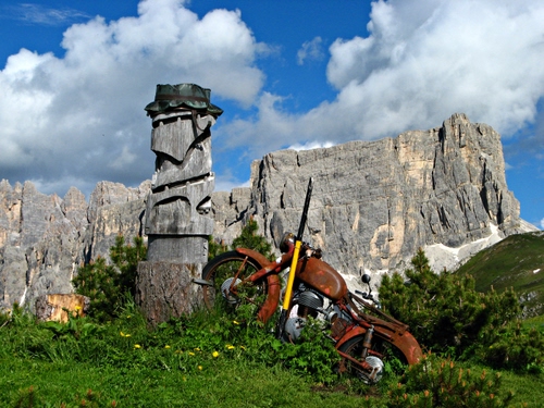 Immagine con nuvole, cielo, montagna, verde, motocicletta, moto, monumento, erba, montagne, rocce, ruggine, ruote, azzurro, legno, alberi, prato, totem, tronco, roccia