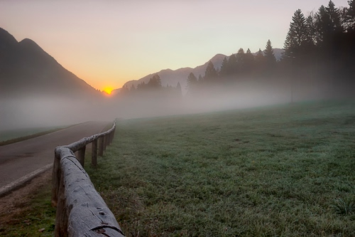 Immagine con nebbia, strada, prato, staccionata, alberi, alba, tramonto, sole, montagna, erba, steccato