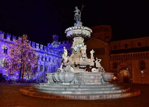Immagine con fontana, statue, albero, piazza, luci, notte, castello, notturno, viola, blu, scalini, merli, nero, colori, tridente, gradini, finestre