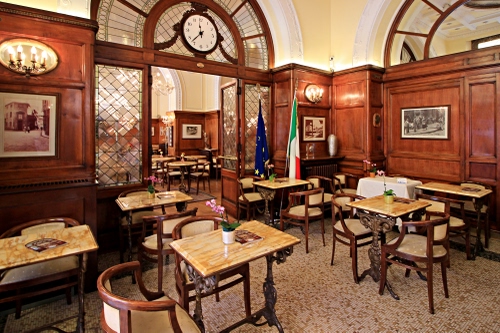 Immagine con orologio, quadri, sedie, tavoli, bandiere, legno, tavolini, interno, fiori, lampade, vetrata, bar, luci, archi, vetri